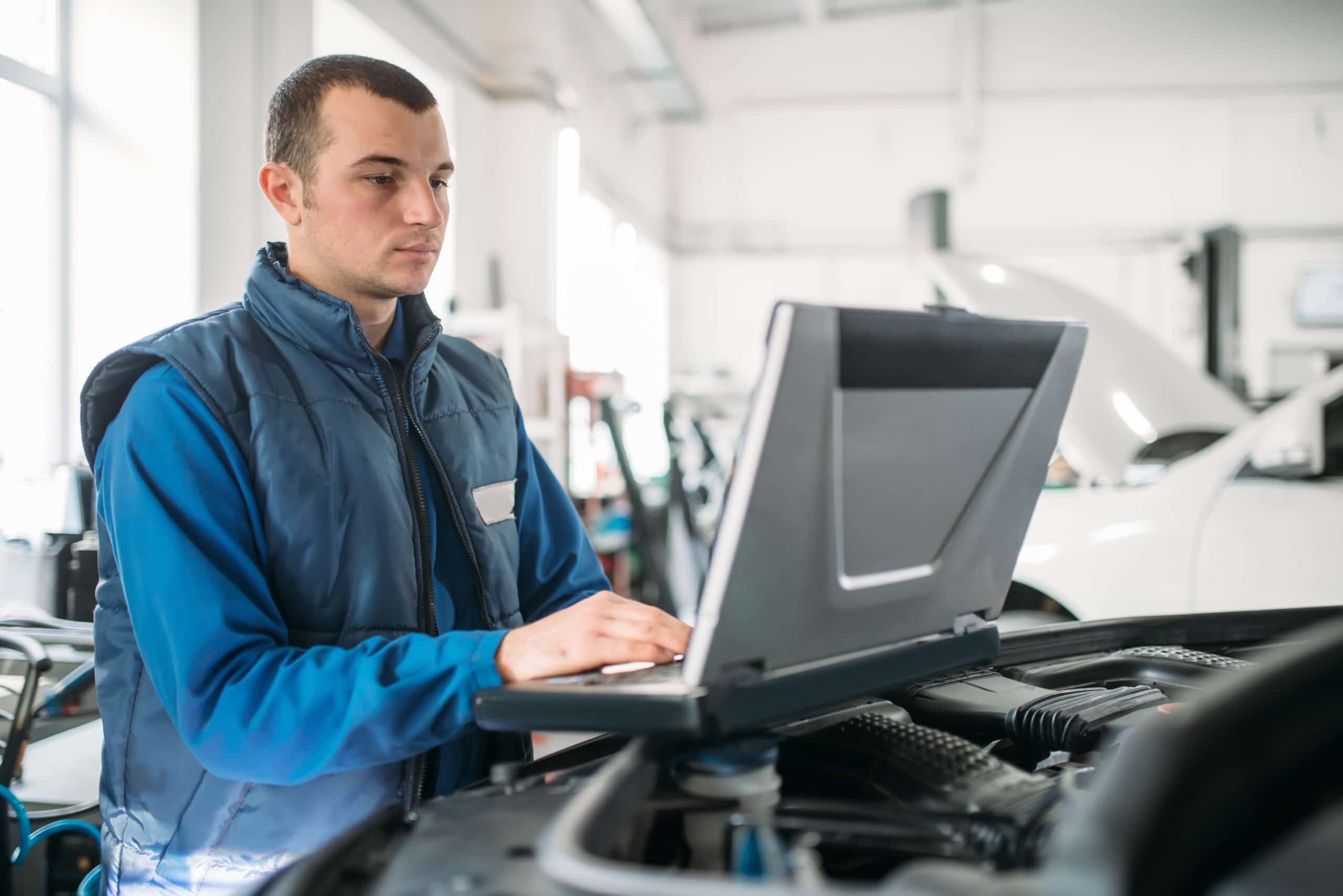 Man at auto dealership on a laptop on top of a car engine
